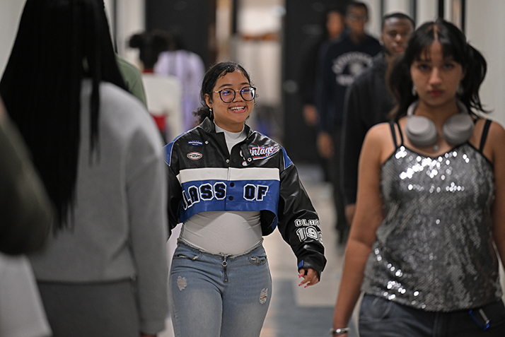 A smiling student walks in a hallway with other students practicing a fashion show strut