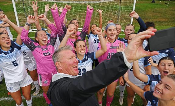 Women's soccer coach and players pose for a group photo on the field.