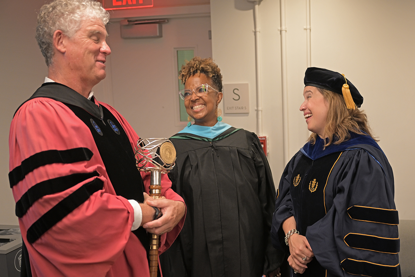 Three academics in robes laugh together.